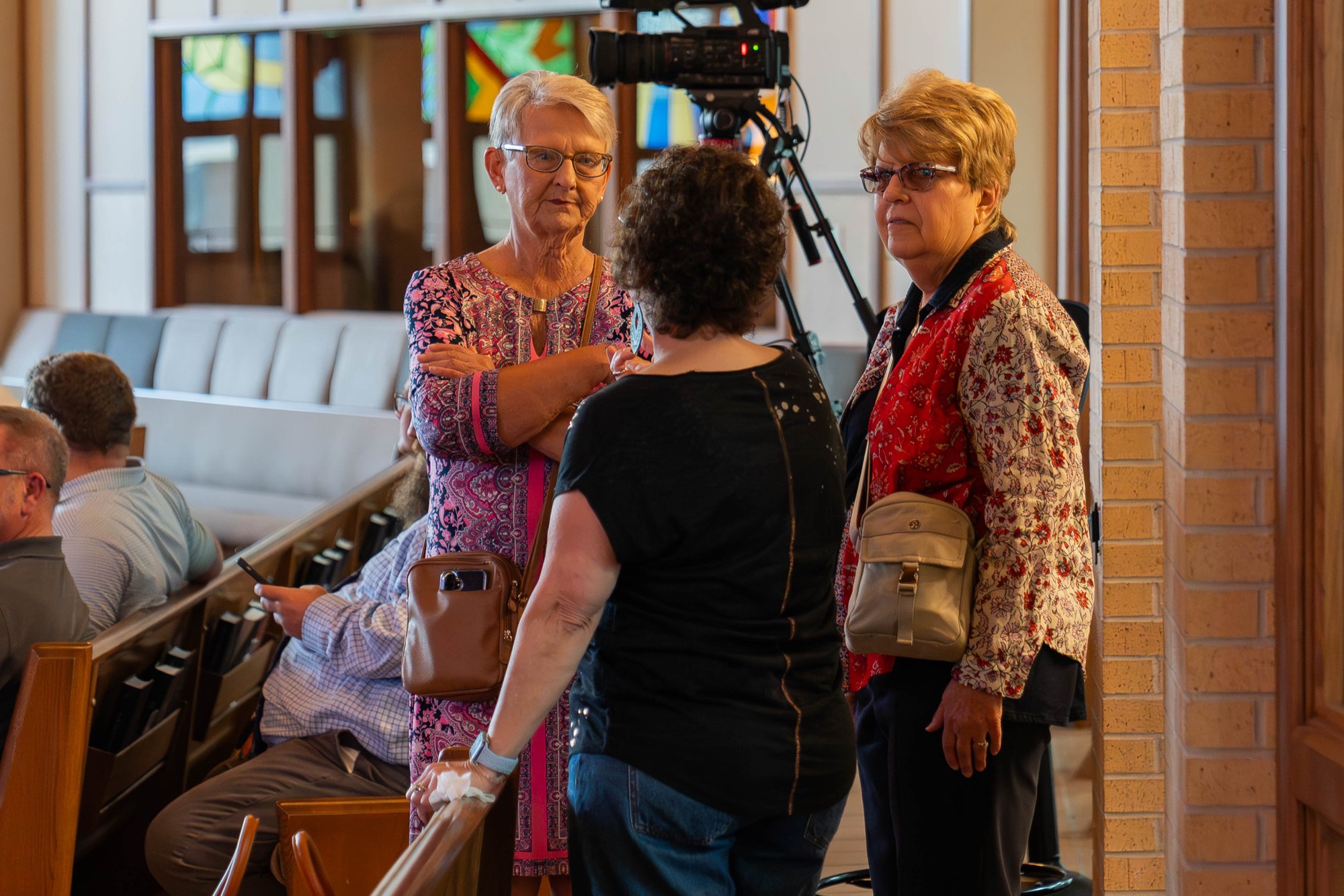Three churchgoers talking, a video camera rigged in the background.