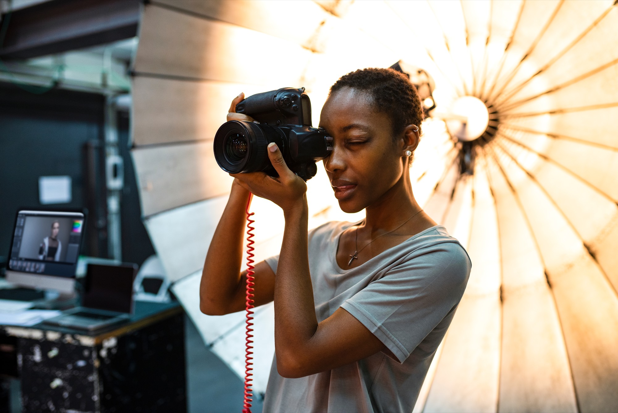 A photographer holds a digital camera in a studio with a large umbrella light behind her