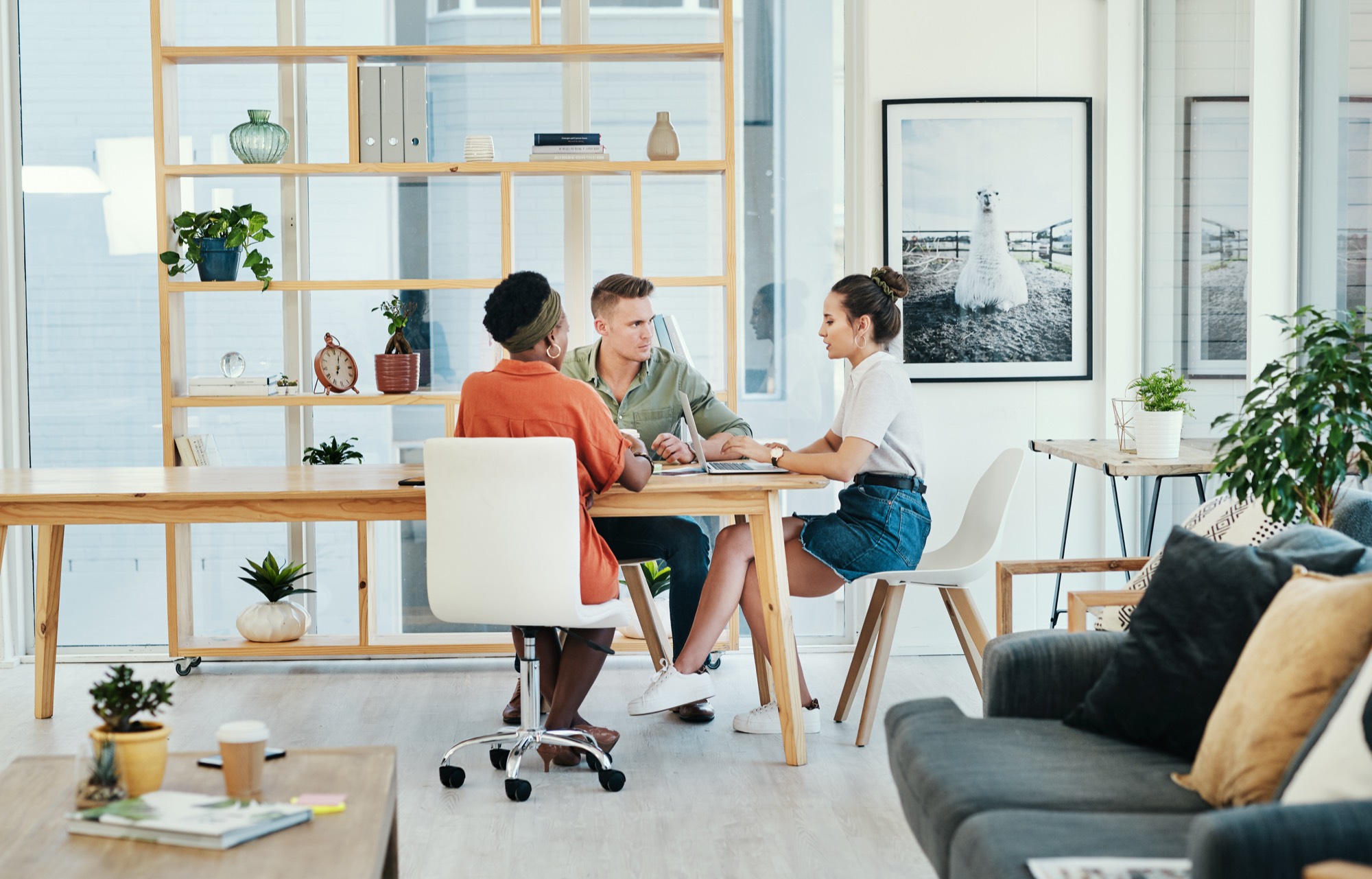 Three coworkers sit around a laptop and review a project in a bright office